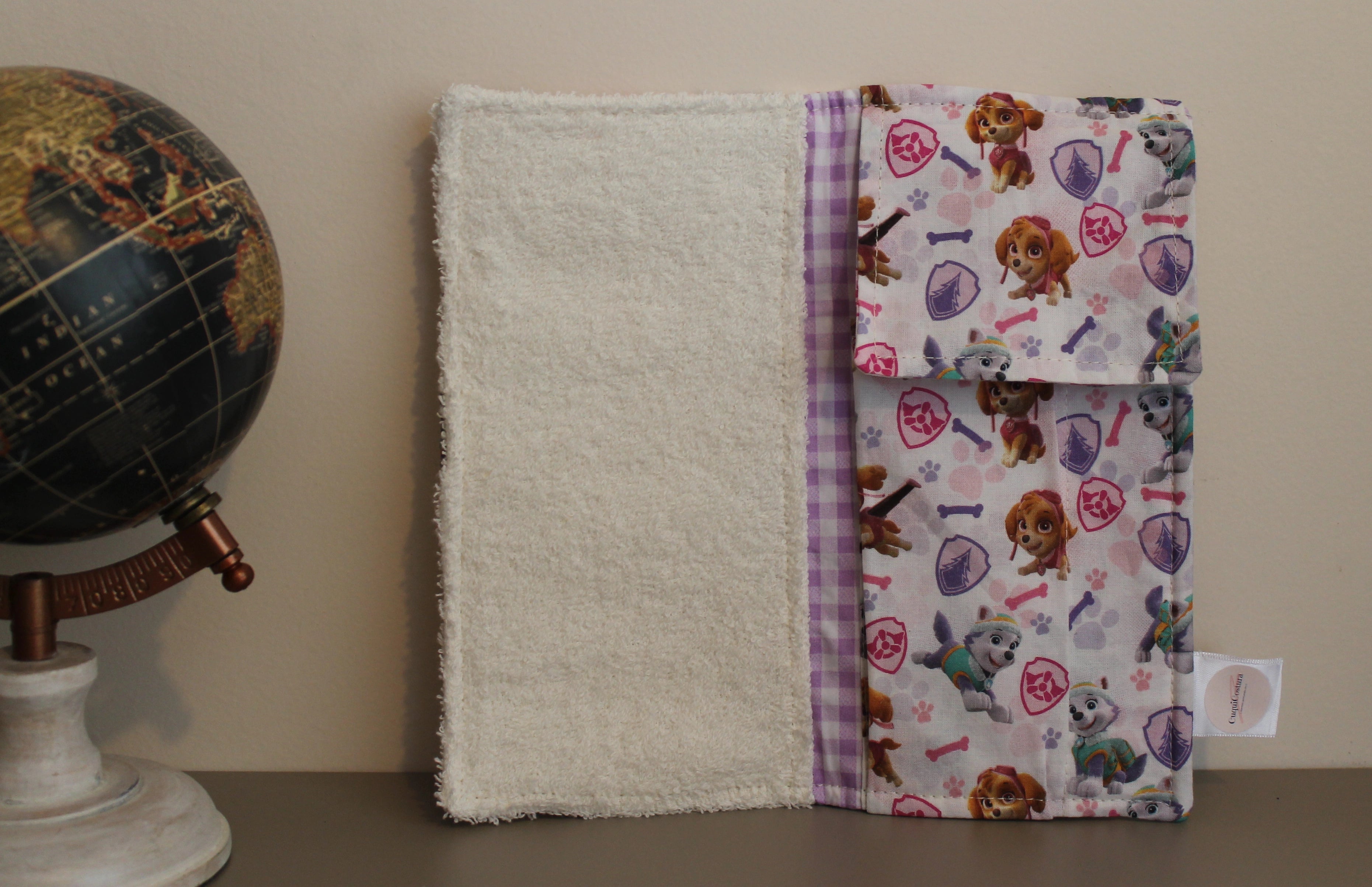 Interior del kit dental infantil con estampado de Skye (Paw Patrol), bolsillo con fondo vichy lila, junto a globo terráqueo