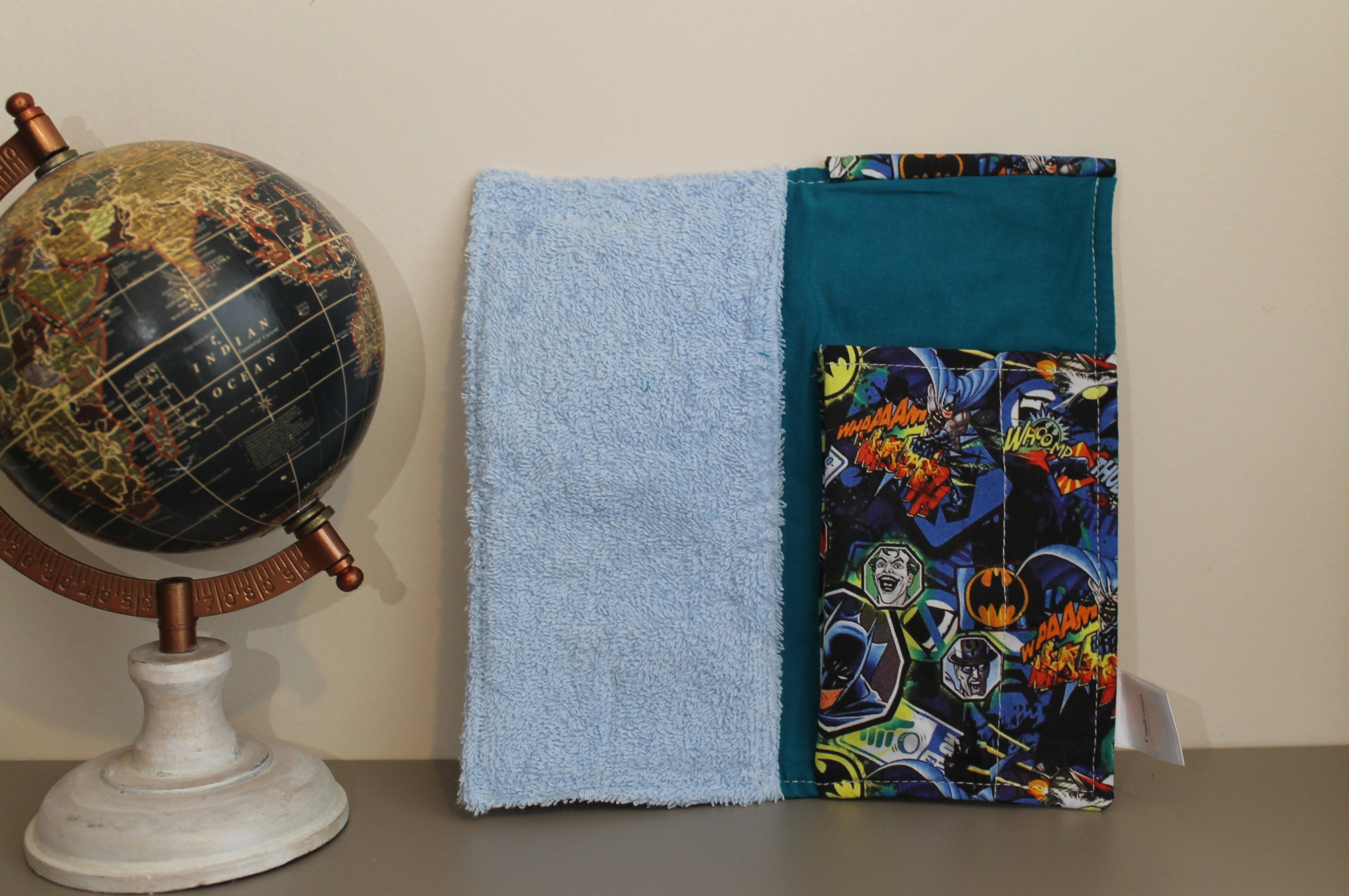 Interior del kit dental infantil con estampado de Batman, Joker y viñetas de cómic, junto a un globo terráqueo sobre fondo beige