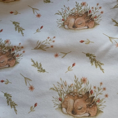 Primer plano de la tela con el estampado de ciervos durmiendo entre ramas y flores sobre fondo claro.