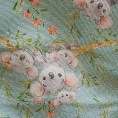 Detalle de la tela estampada con koalas grises abrazados entre flores y ramas sobre fondo azul.