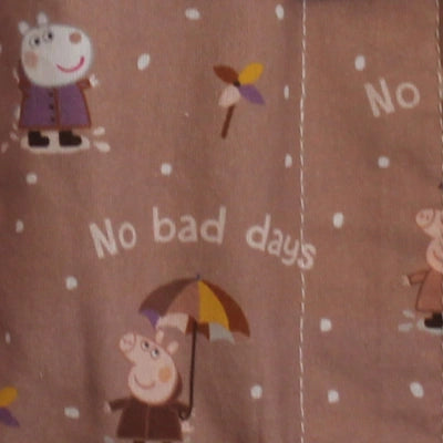 Detalle del estampado infantil de Peppa Pig bajo la lluvia con paraguas y mensaje "No bad days" sobre fondo marrón rosado