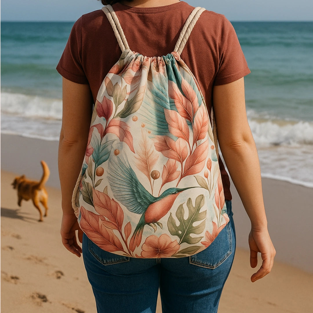 Mujer de espaldas con mochila de cuerdas artesanal estampada con colibrí y hojas tropicales, en la playa.