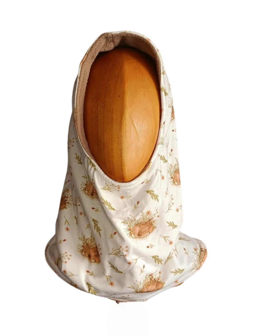 Buff’n’hood infantil con capucha, estampado de ciervos durmiendo entre flores silvestres, visto desde el frente sobre maniquí de madera.Buff’n’hood infantil con capucha, estampado de ciervos durmiendo entre flores silvestres, visto desde el frente sobre maniquí de madera.