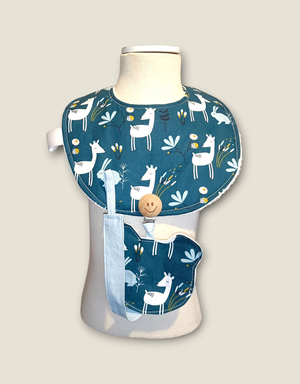 Babero impermeable y chupetero del Pack Mini Yo – Esenciales de Bebé Ciervo Flor Azul presentados en maniquí.