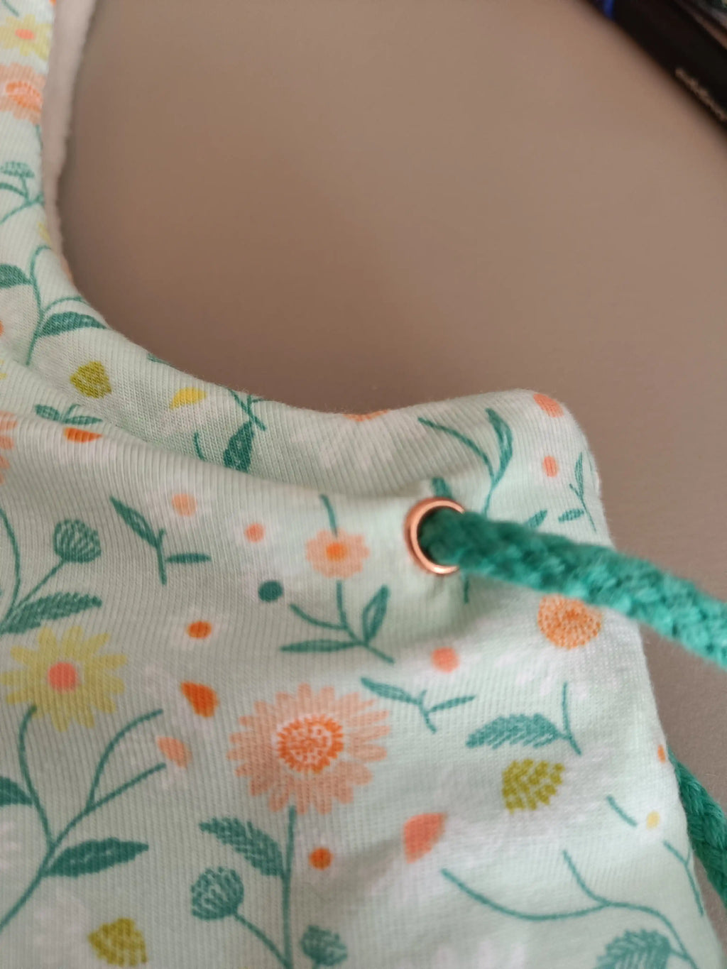 Primer plano de ojales y cordón en Buff’n’hood infantil con estampado de girasoles.