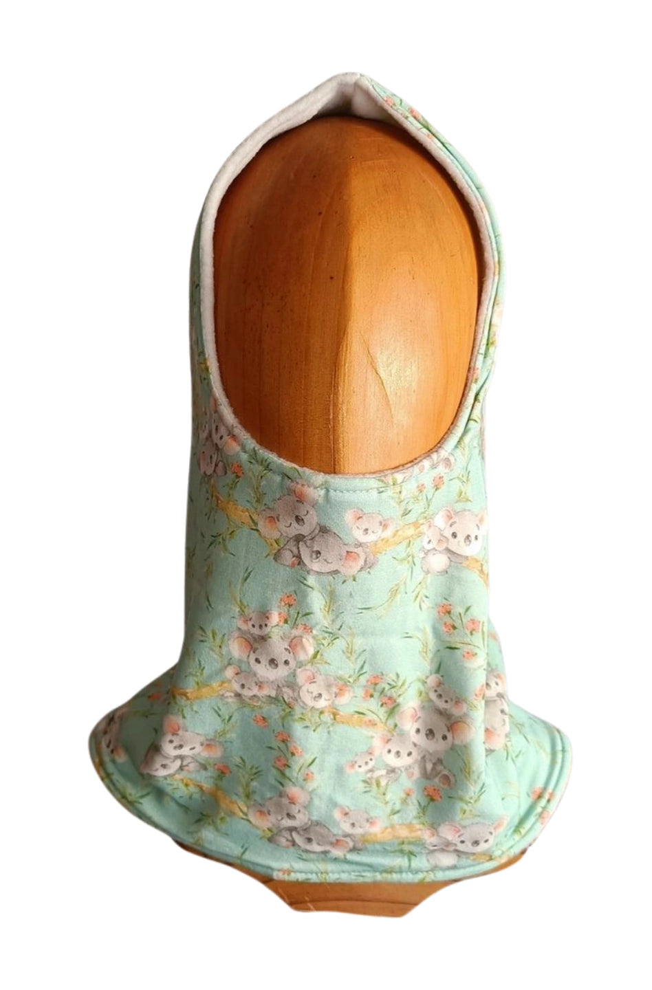 Buff’n’hood artesanal con capucha, estampado de koalas sobre fondo azul y forro blanco, visto de frente sobre cabeza de madera.