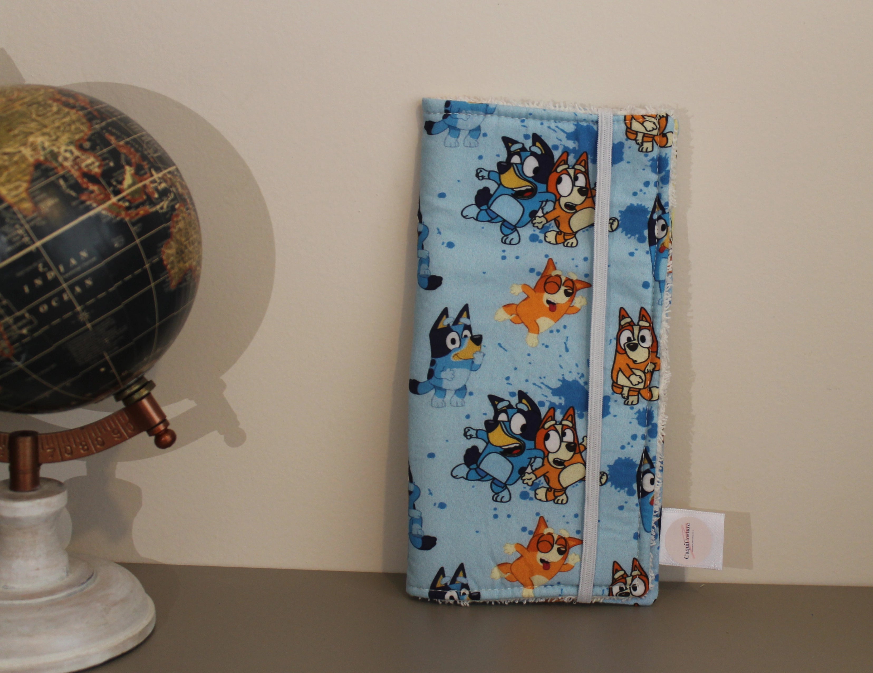 Estuche dental infantil artesanal con estampado de Bluey, cerrado, junto a un globo terráqueo sobre fondo beige