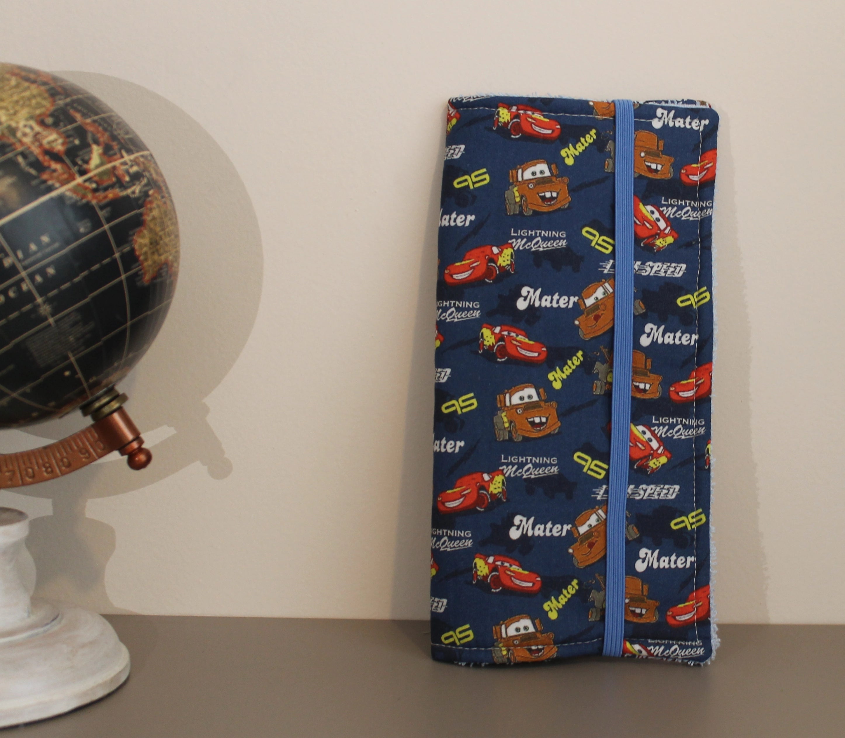 Estuche dental infantil cerrado con estampado de Cars, junto a globo terráqueo sobre fondo beige