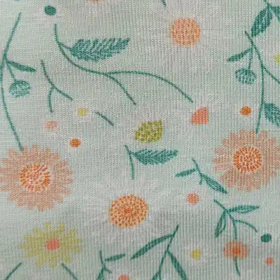 Muestra de tela estampada con flores girasol en tonos pastel sobre fondo verde agua.