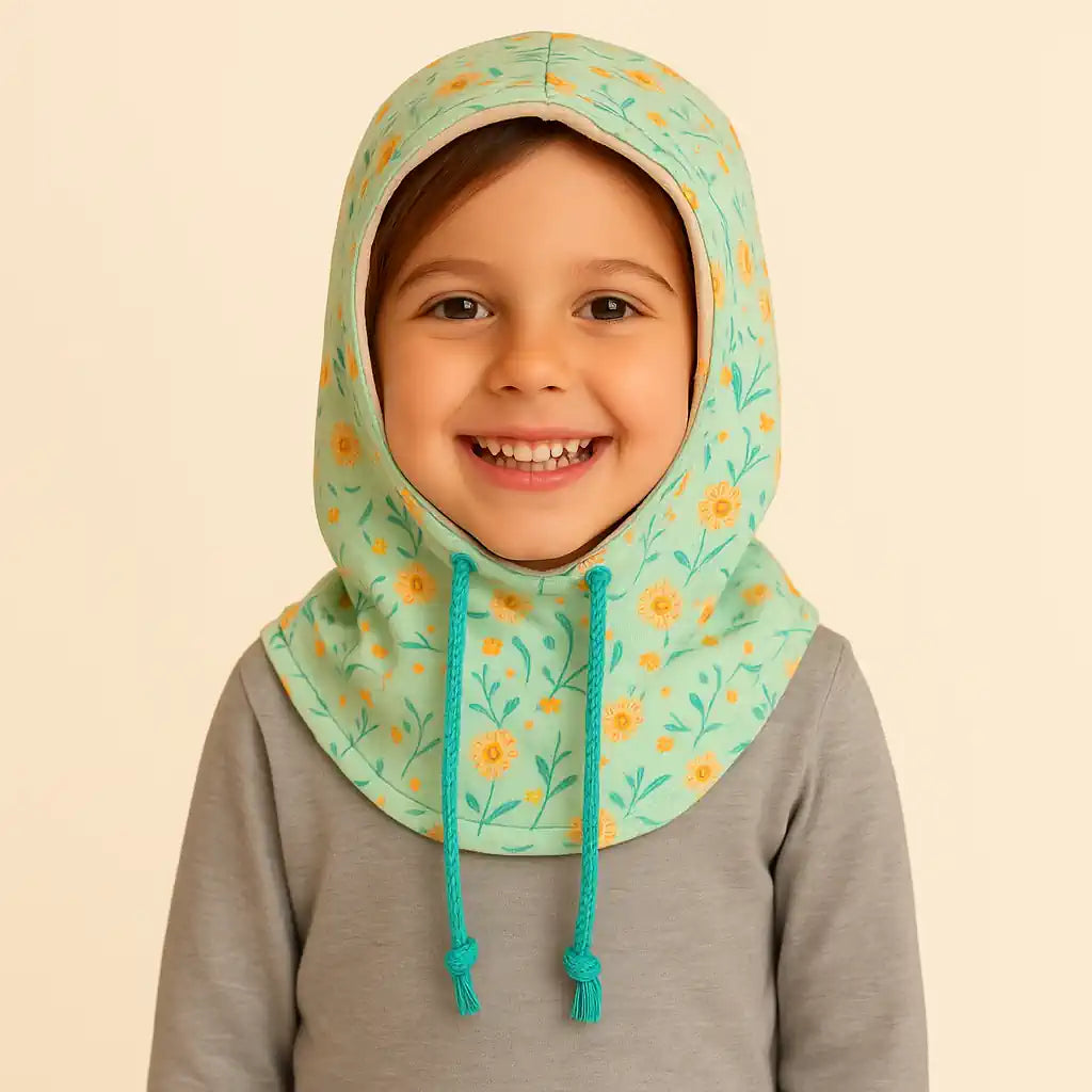 Niña sonriendo con Buff’n’hood infantil reversible de girasoles y cordón ajustable.